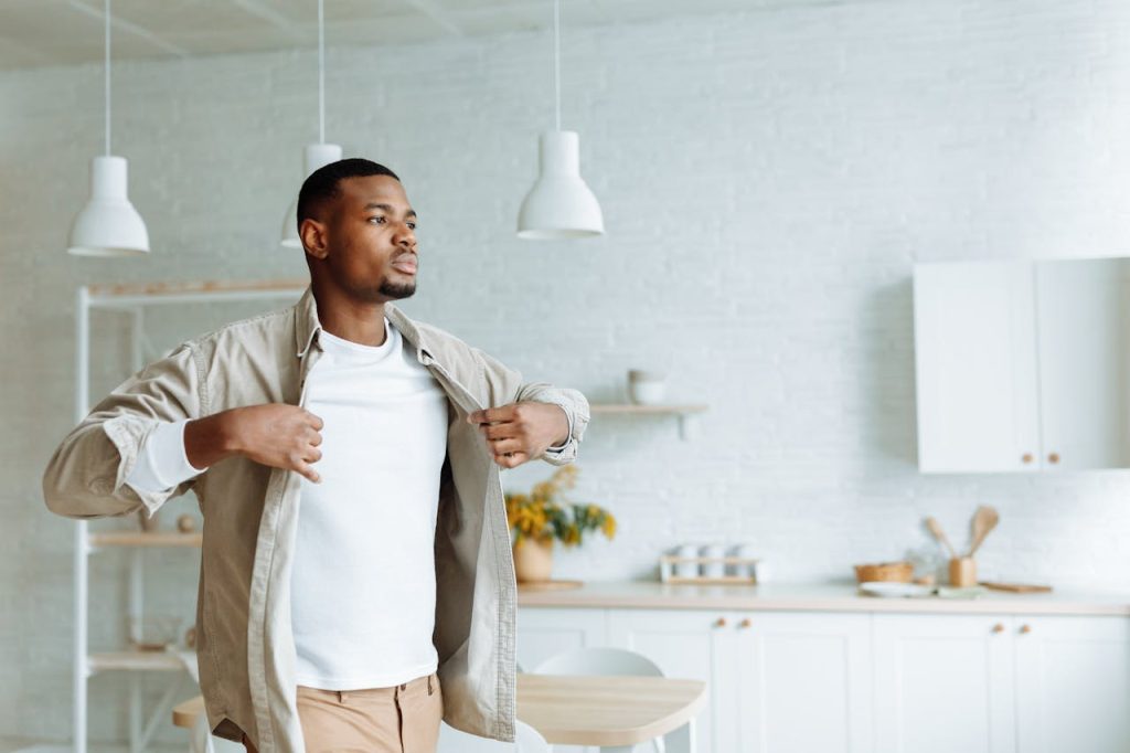 A confident man standing in a bright kitchen, opening his shirt slightly with a calm and grounded expression, symbolizing emotional authenticity and healthy masculinity.