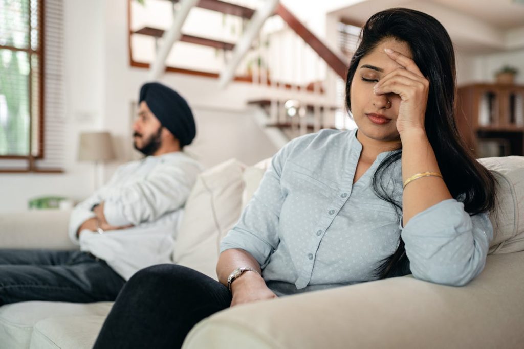 A couple sitting on opposite ends of a couch, both looking away, illustrating emotional distance and communication breakdown in relationships.