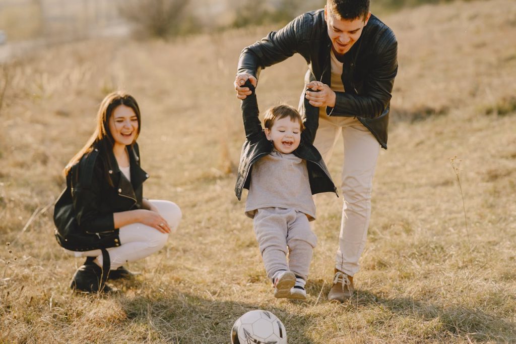 Father lifting his young child while the mother smiles nearby during outdoor family playtime.