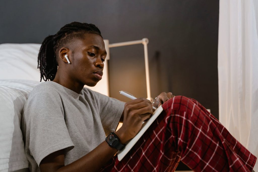 Young man journaling on the floor while reflecting on his emotions during a quiet evening.