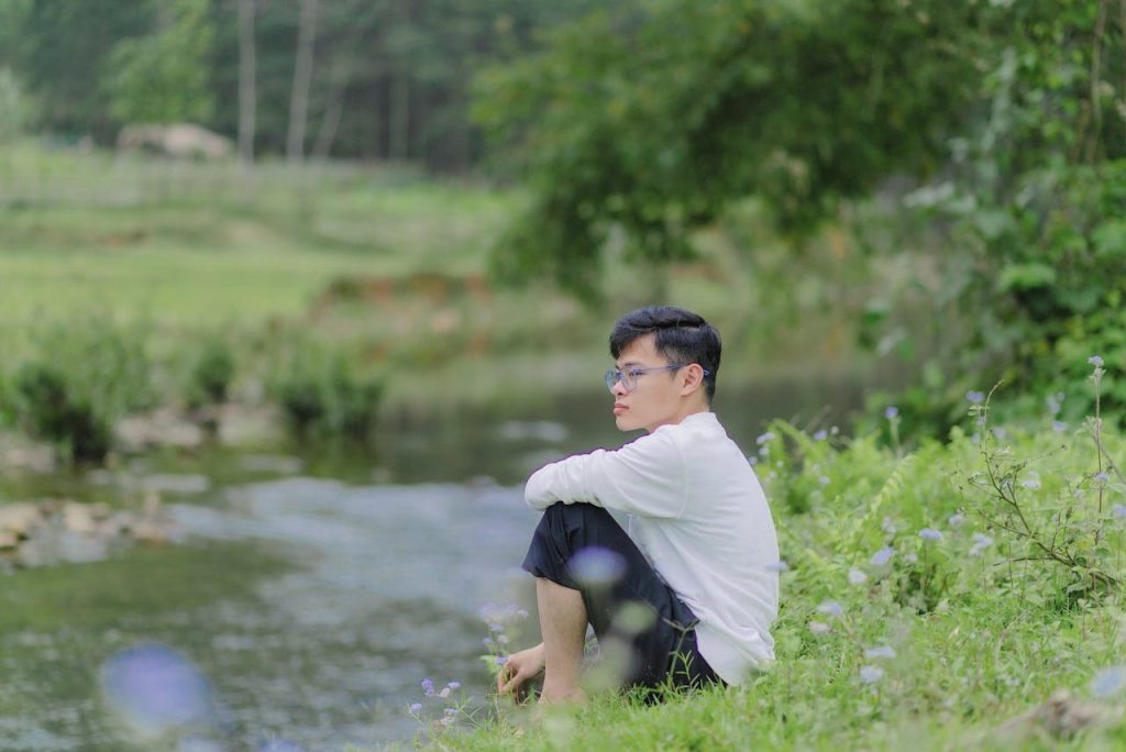 Man sitting alone by a quiet riverside, reflecting in nature during a peaceful moment of silence.