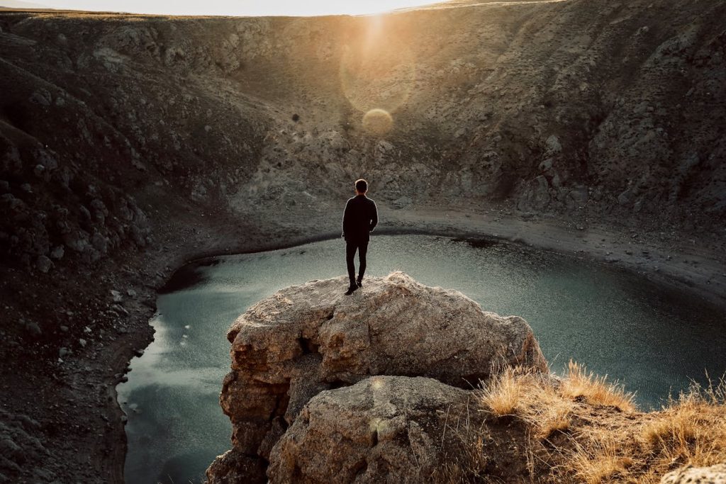 Man standing alone on a cliff overlooking a quiet lake at sunrise, symbolizing reflection and the power of silence.
