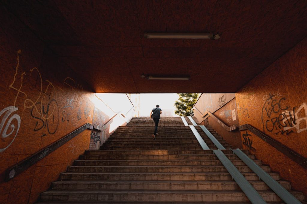 Man running up a staircase toward daylight in an urban underpass, symbolizing breaking free from toxic peer pressure.