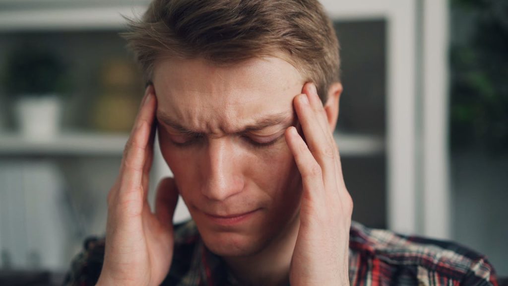 Man rubbing his temples in visible discomfort, symbolizing the physical impact of suppressed emotions and emotional stress.