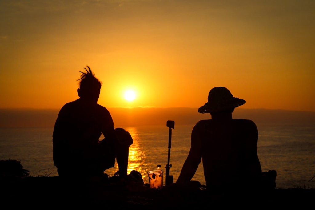 Two men sitting together on a cliff at sunset, silhouetted against the ocean, symbolizing male friendship, emotional connection, and meaningful conversations.