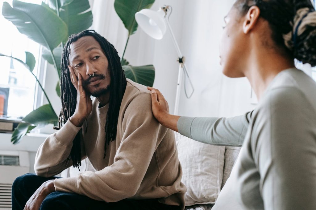 Woman gently comforting a distressed man on a couch, showing emotional support and encouraging open communication.