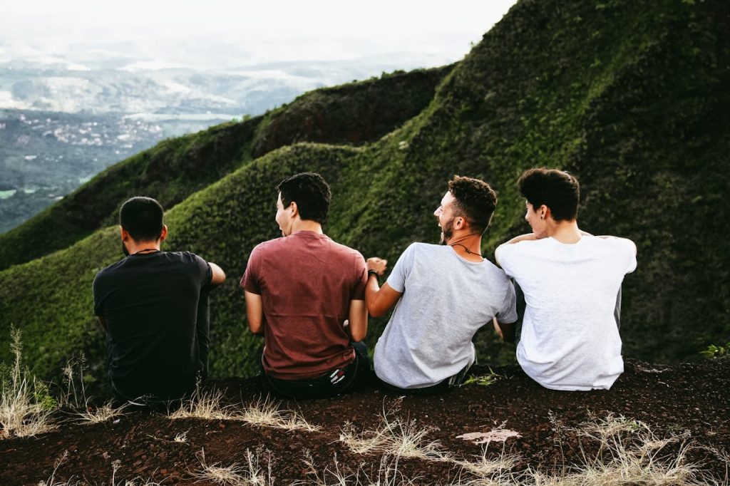Group of young men sitting together on a mountain ridge, sharing a moment of connection and laughter during an outdoor rite-of-passage experience.