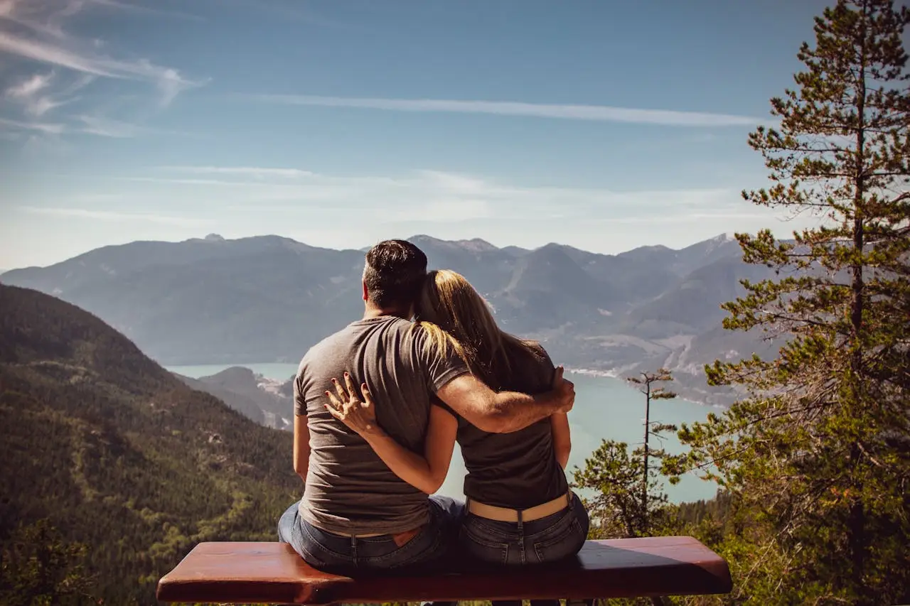 Couple sitting together overlooking mountains and a lake, symbolizing emotional connection and the supportive role women play in healthy masculinity.