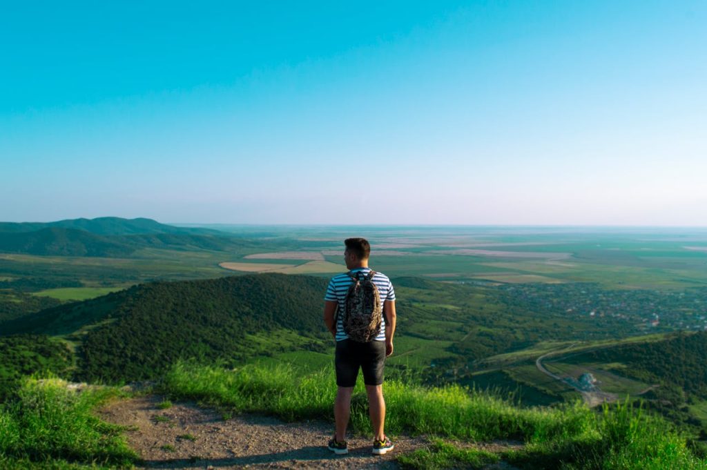 Man standing on a mountaintop, looking toward an open landscape and horizon, symbolizing the freedom to define identity beyond work.