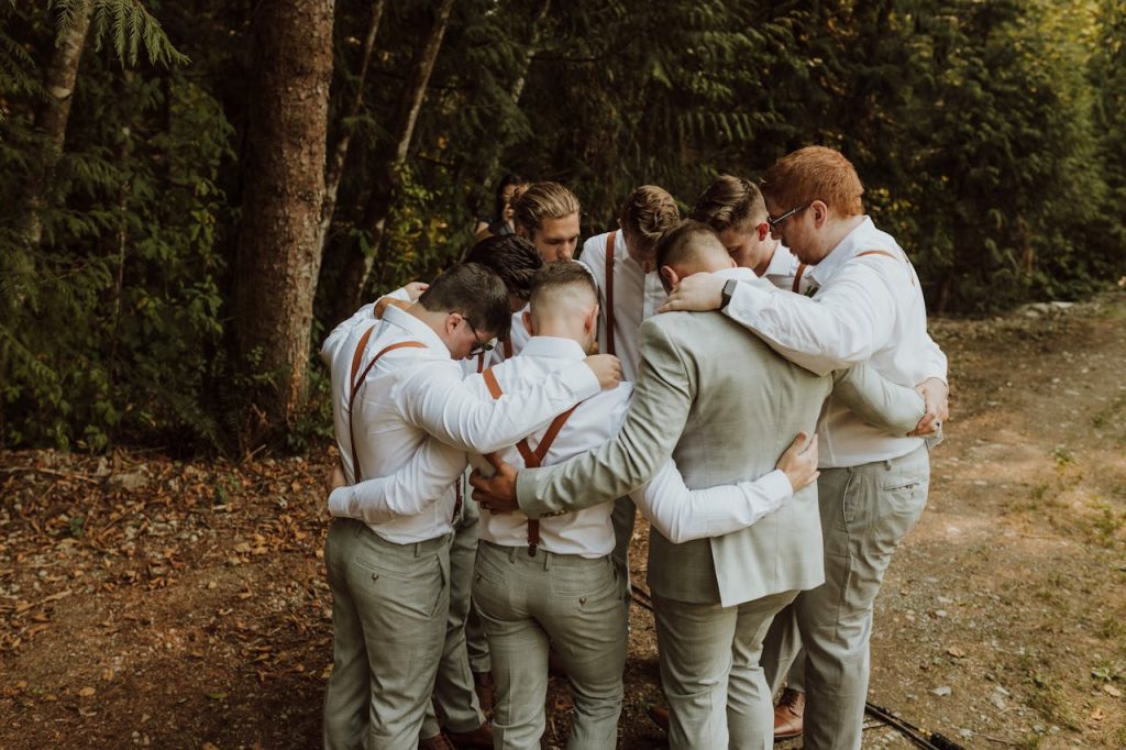 A group of men standing in a tight circle outdoors with their arms around each other, symbolizing the importance of male support groups and emotional brotherhood.