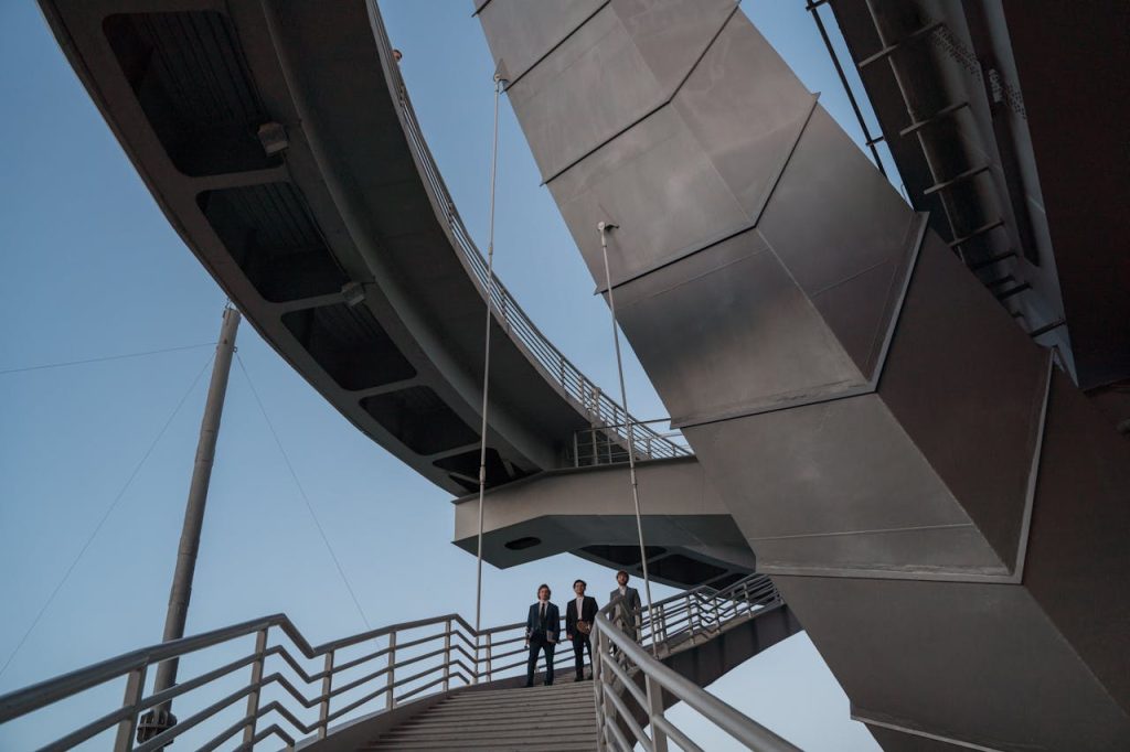 Men in business suits standing beneath towering corporate architecture, appearing small against the massive structures, symbolizing how work can overshadow personal identity.