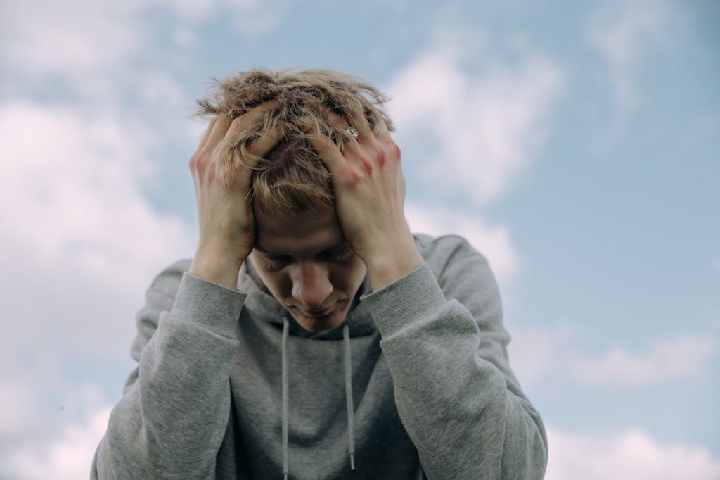 A distressed young man holding his head in his hands outdoors, illustrating emotional overwhelm and the weight of unprocessed stress.