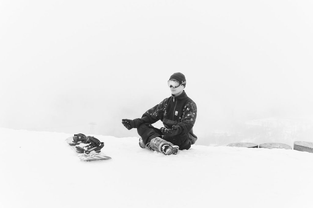 Athlete meditating in the snow beside his snowboard, practicing mindfulness and inner peace.
