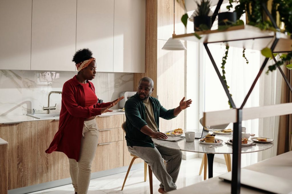 Couple arguing in a kitchen while the man works on a laptop during breakfast, highlighting tension caused by blurred work–life boundaries.