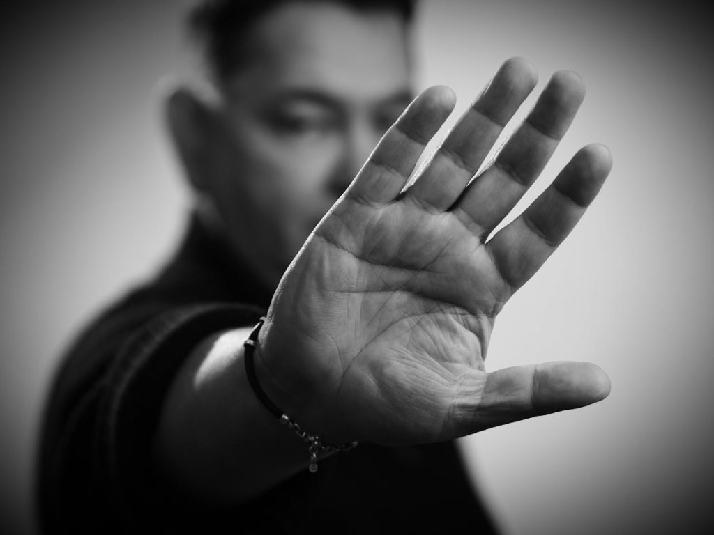 A man holding his hand forward in a clear stop gesture, symbolizing setting boundaries and protecting emotional well-being during distress.