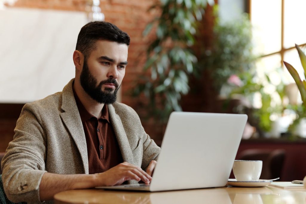 Focused man working calmly on a laptop in a café, representing the balance between ambition and inner peace.