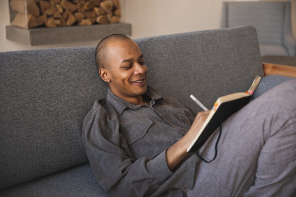 Man relaxing on a couch while journaling, practicing self-reflection and personal identity check-ins separate from his work role.