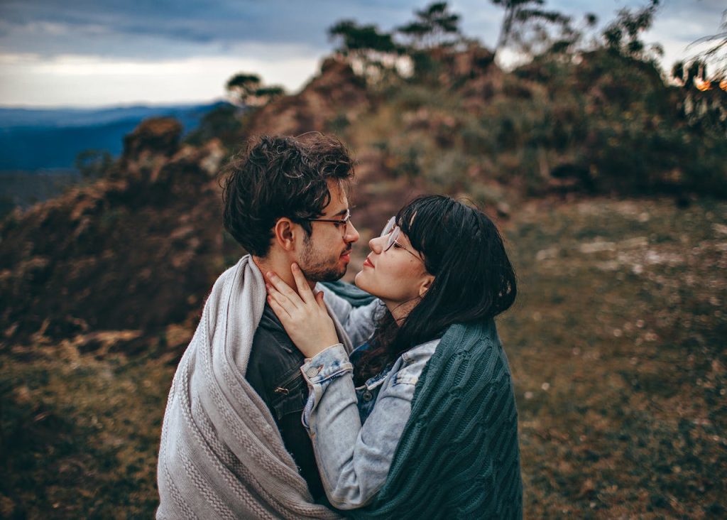 Couple wrapped in blankets embracing outdoors, sharing a quiet moment of eye contact that reflects emotional presence and authentic connection.