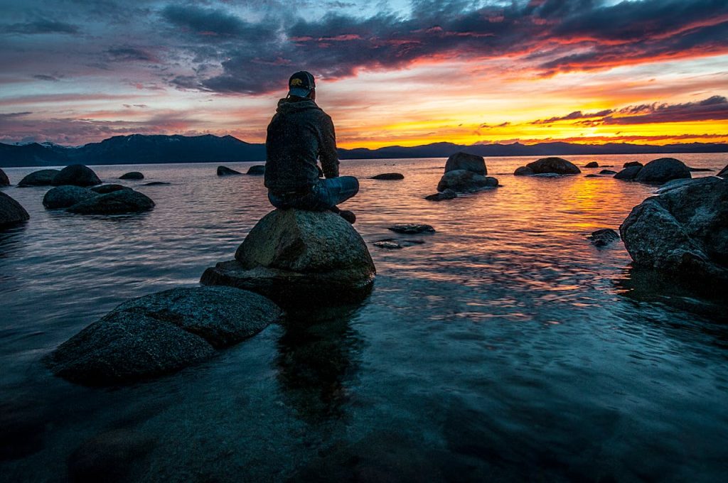 Man sitting alone on a rock by a lake during sunset, reflecting quietly and symbolizing self-discovery beyond work identity.