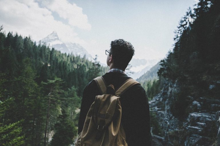 Man standing alone in nature with a backpack, looking at distant mountains—symbolizing the value of boredom, stillness, and unplugging for renewed creativity.