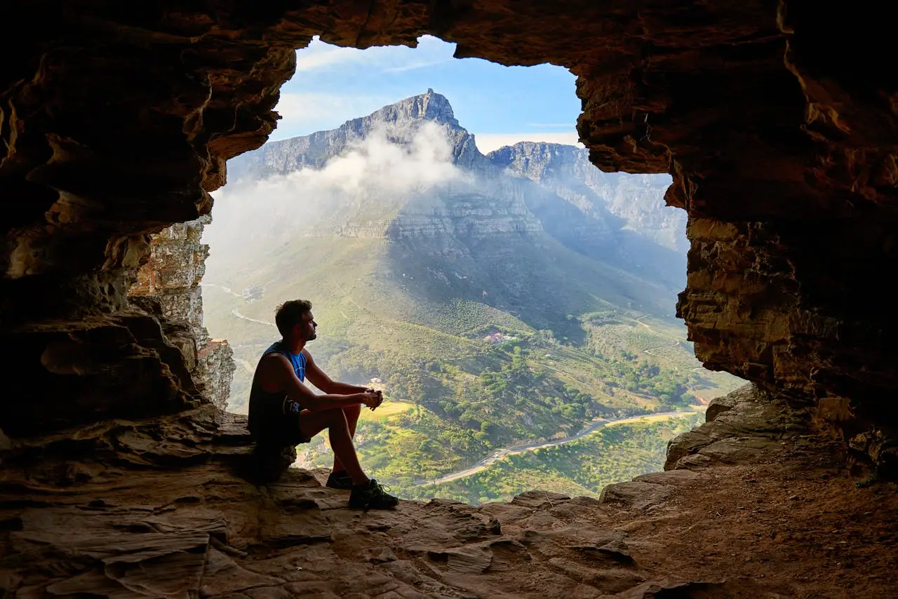 Man sitting inside a rocky cave overlooking a vast mountain landscape, symbolizing men’s inner reflection and personal growth.