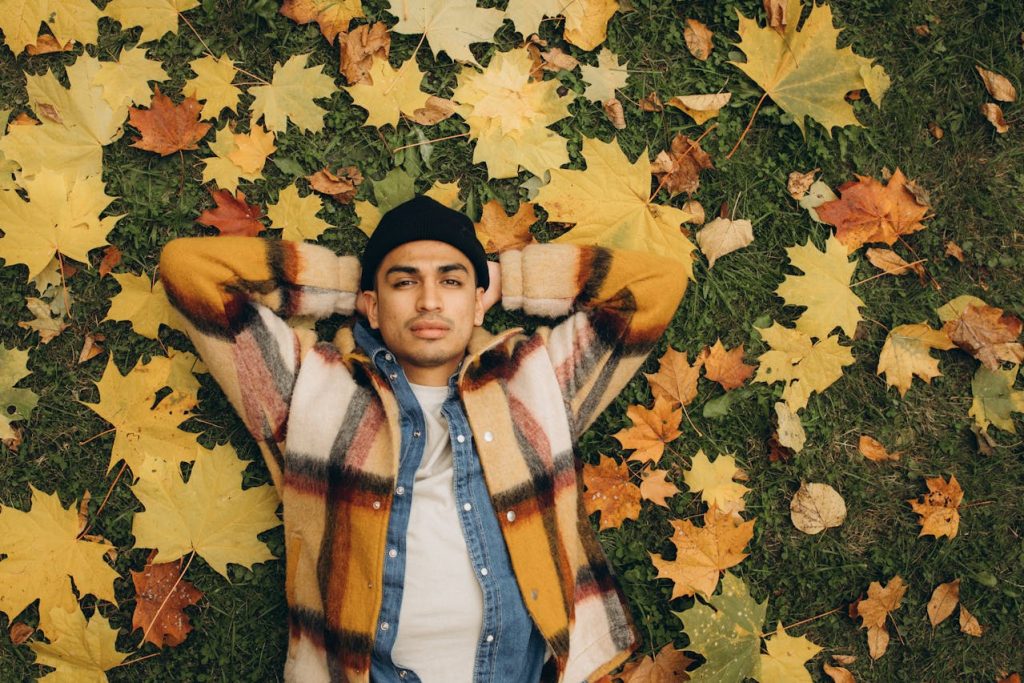 Man lying on autumn leaves with hands behind his head, resting and unplugging outdoors to embrace restorative boredom.