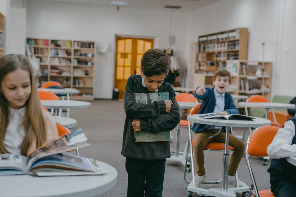 Boy standing alone in a classroom while another child points and mocks him, illustrating early toxic peer influence and social pressure.