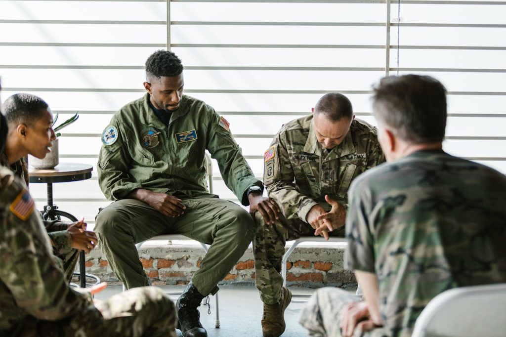 Military men sitting in a support circle, one soldier comforting another who appears distressed, symbolizing emotional struggle and peer support.