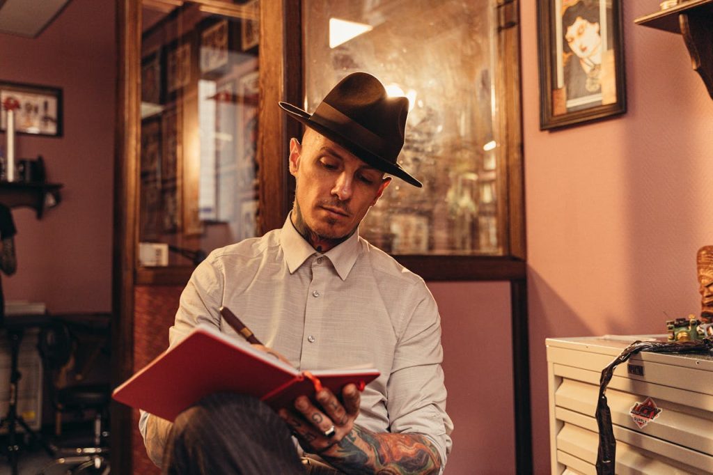 A man with tattoos and a fedora writing in a journal, symbolizing self-reflection and emotional processing for men.