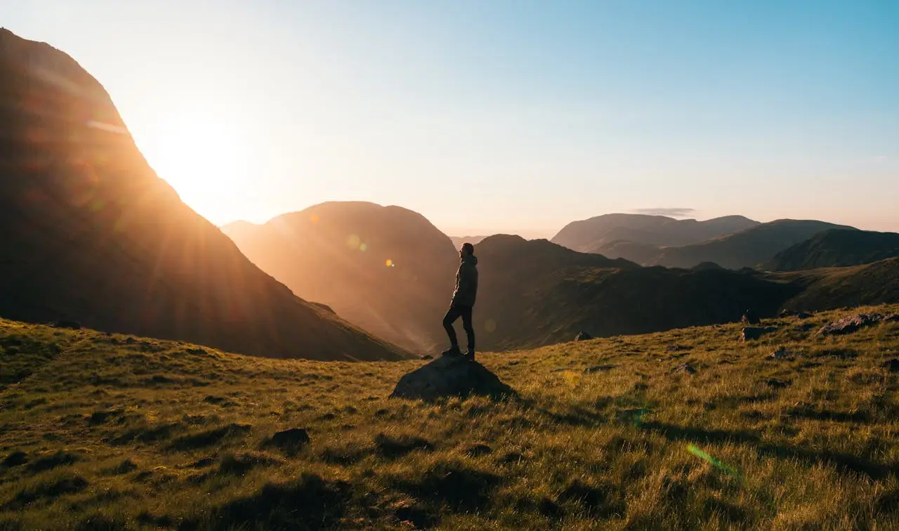 Man standing on a rock at sunrise overlooking wide mountain valleys, symbolizing the ongoing journey of growth, purpose, and masculine development.