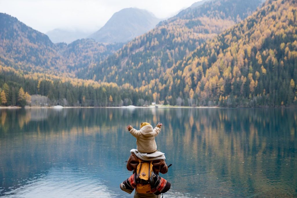 Father holding his child while sitting by a mountain lake, modeling healthy emotional connection and positive male role-modeling.