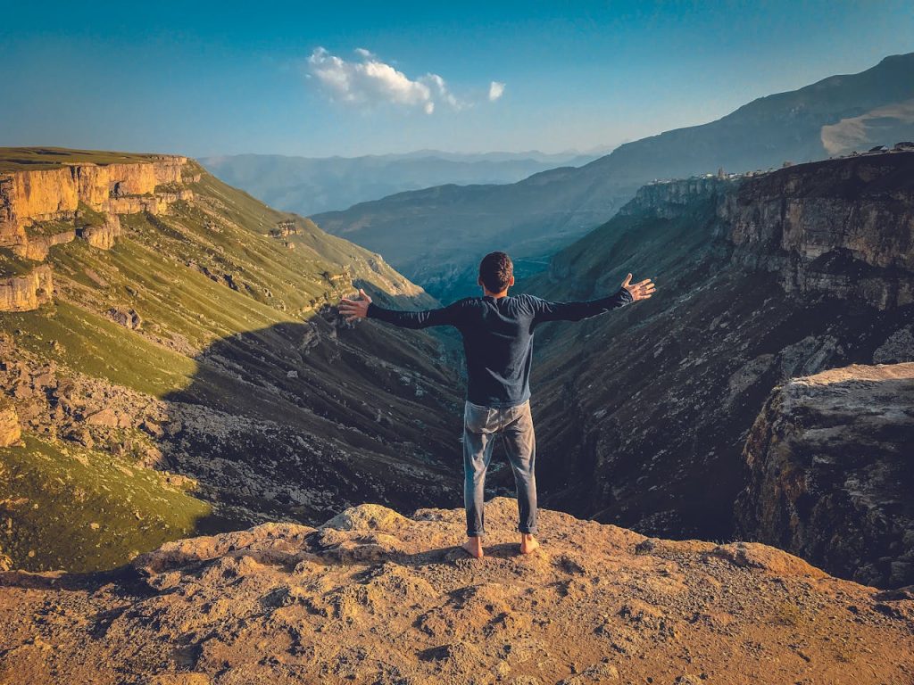 Man standing barefoot on a mountain peak with arms open, symbolizing accomplishment and inner peace.