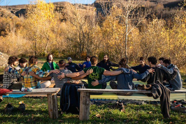 Men sitting in a supportive outdoor circle with arms around each other, symbolizing male community, emotional connection, and the importance of brotherhood.