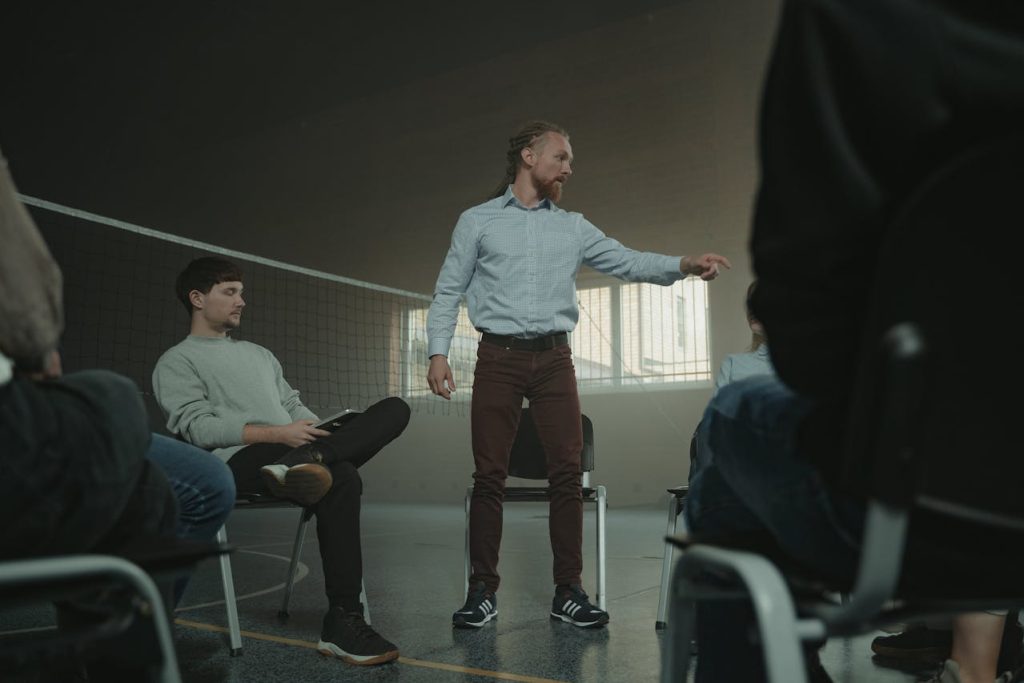 A facilitated men’s support group with one man standing and speaking while others listen in a circle—representing the importance of male support groups and structured emotional support.