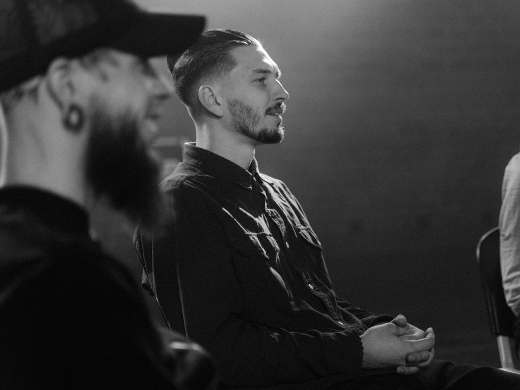 Men sitting together in a support group, one man speaking while others listen attentively—representing the importance of male support groups and emotional connection.