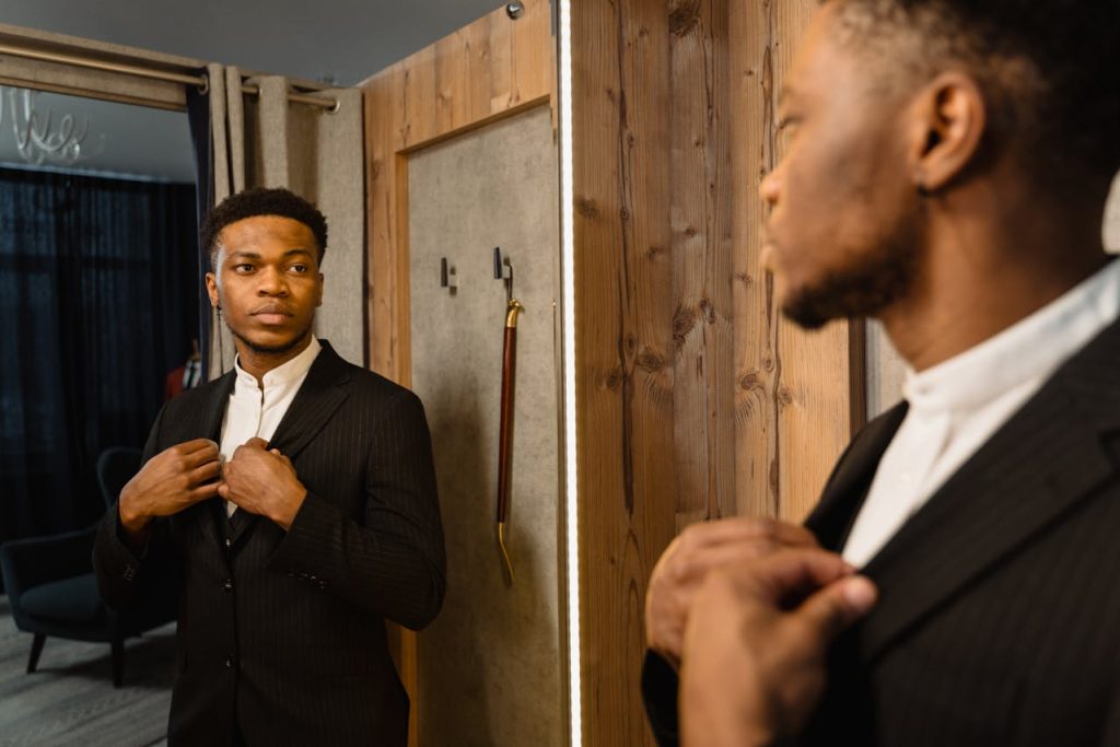 Man adjusting his suit while looking confidently in the mirror, symbolizing self-worth and inner peace beyond external achievement.