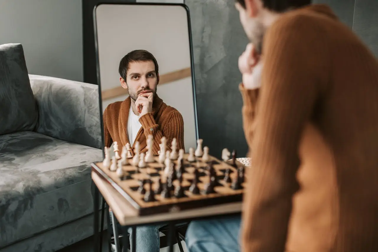 Man reflecting on himself in a mirror while sitting at a chess table, symbolizing self-awareness and inner inquiry.