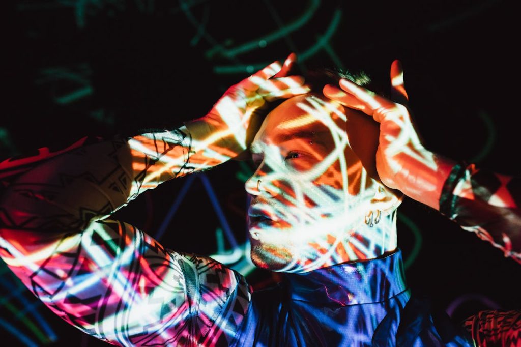Man holding his head with abstract light patterns projected on his face, symbolizing the neurological stress response linked to childhood trauma and men’s mental health.