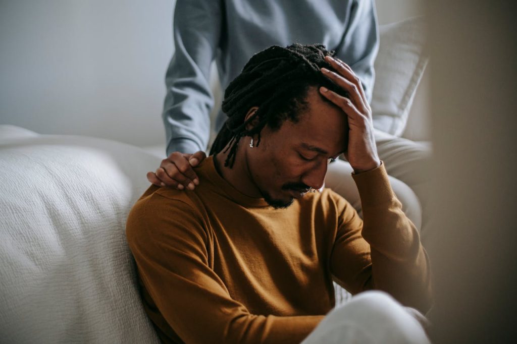 Man sitting with his head in his hand while someone offers support, symbolizing how avoiding help turns small problems into overwhelming emotional crises.