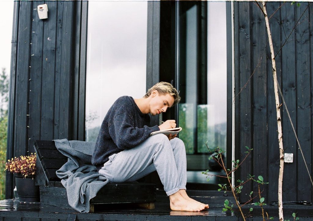Man journaling outdoors on a cabin porch, reflecting quietly as part of a self-discovery practice.