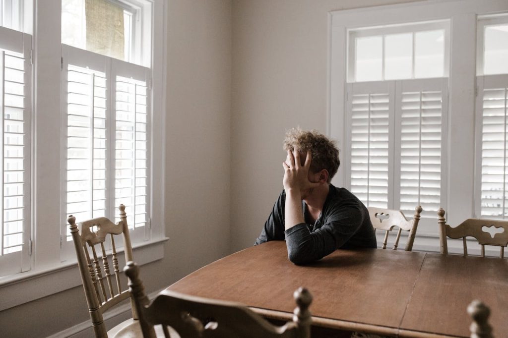 Man sitting alone at a table with his hand covering his face, expressing isolation and emotional overwhelm linked to the strong silent archetype.