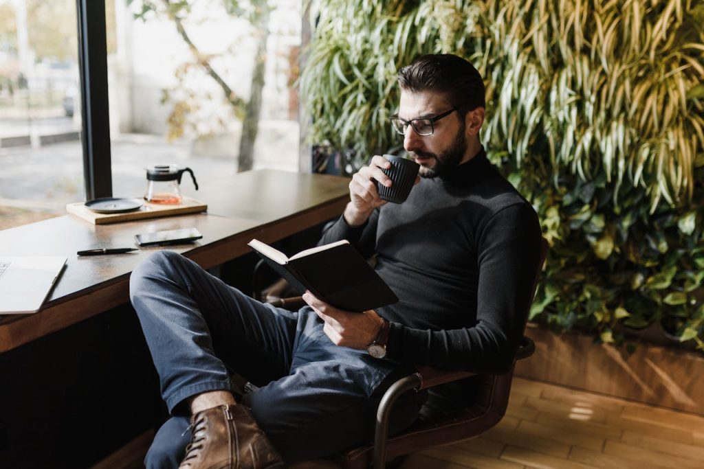 Man reading a book and drinking coffee in a calm, cozy indoor space.
