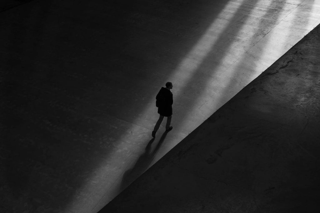 A lone man walking through darkness into a beam of light, symbolizing shadow work for men and the confrontation of hidden aspects of the self.