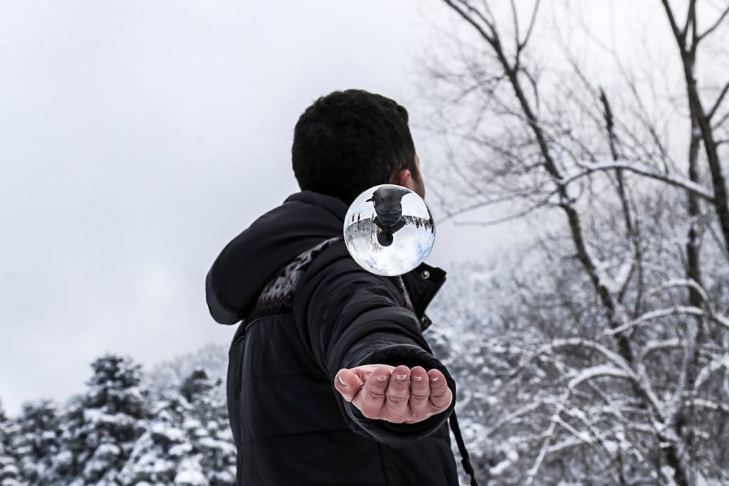 Man standing outdoors in winter balancing a reflective sphere in his hand, symbolizing grounded strength and open self-awareness.