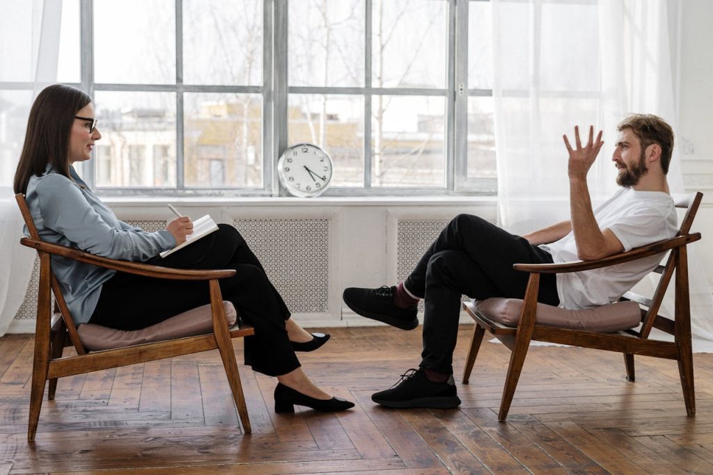 Man in a therapy session having an open, connected conversation with a female therapist in a bright, calm office.