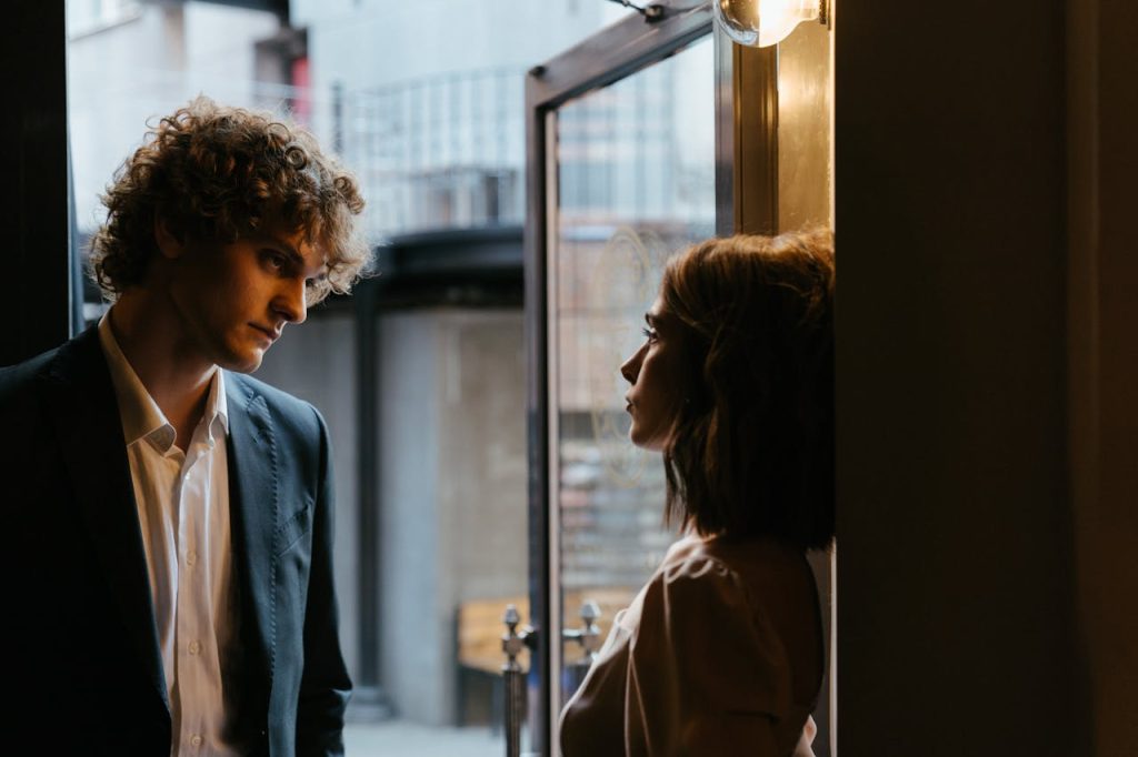 A man speaking vulnerably with a woman in a doorway, showing calm confidence and emotional honesty.