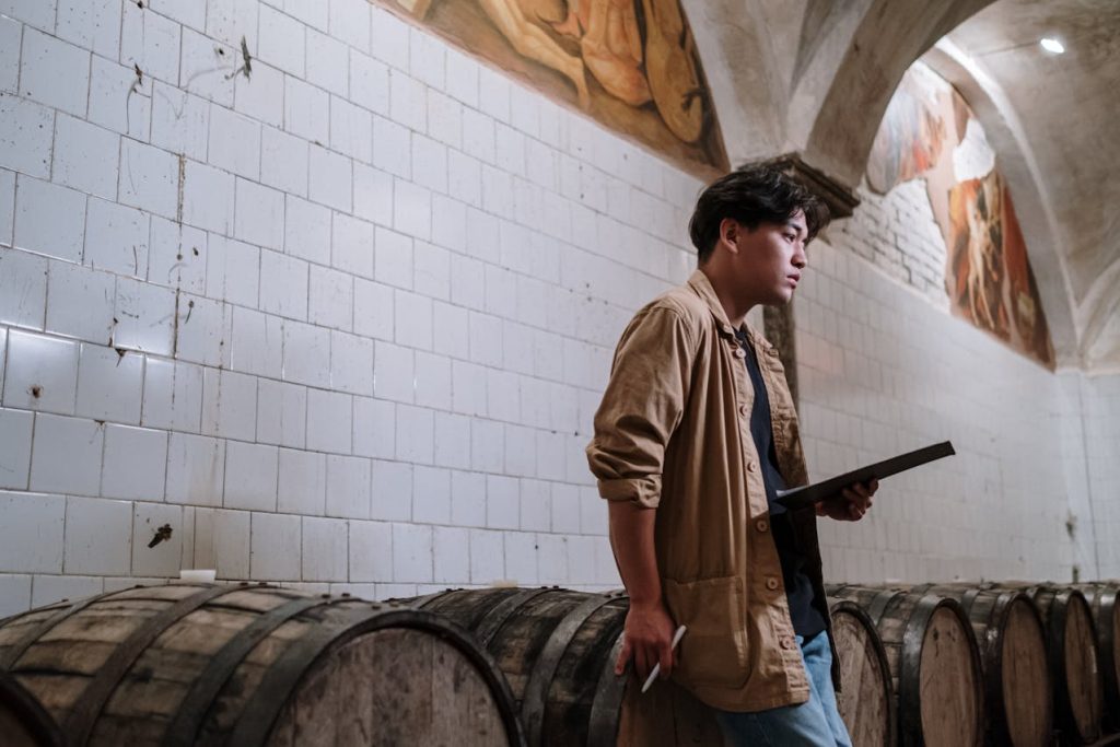 Man standing thoughtfully beside wooden barrels while holding a notebook, symbolizing self-reflection and evaluating different dimensions of personal strength.