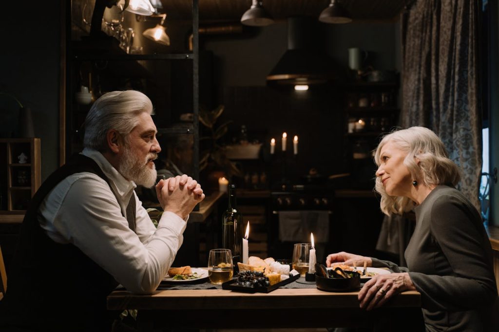 Older man with a calm, wise demeanor sharing a candlelit dinner and meaningful conversation, symbolizing mature and multidimensional masculine strength.