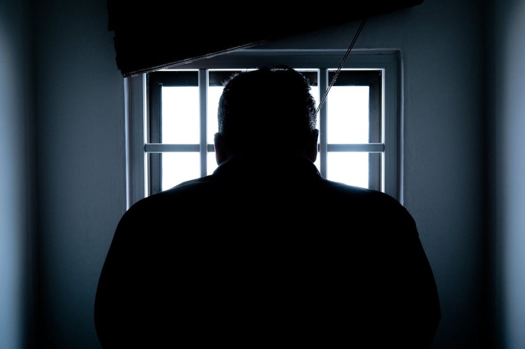 Silhouette of a man standing in darkness before prison-like bars, symbolizing the mental prison created by unhealed masculinity.