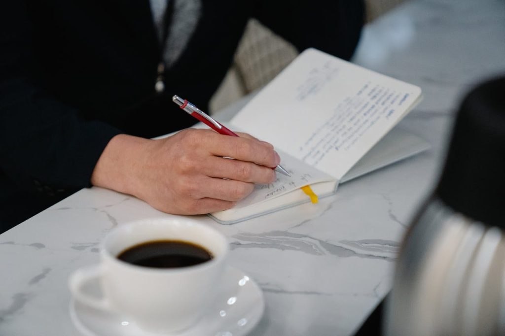 Close-up of a man writing reflective notes in a journal beside a cup of coffee, symbolizing journaling for self-discovery.